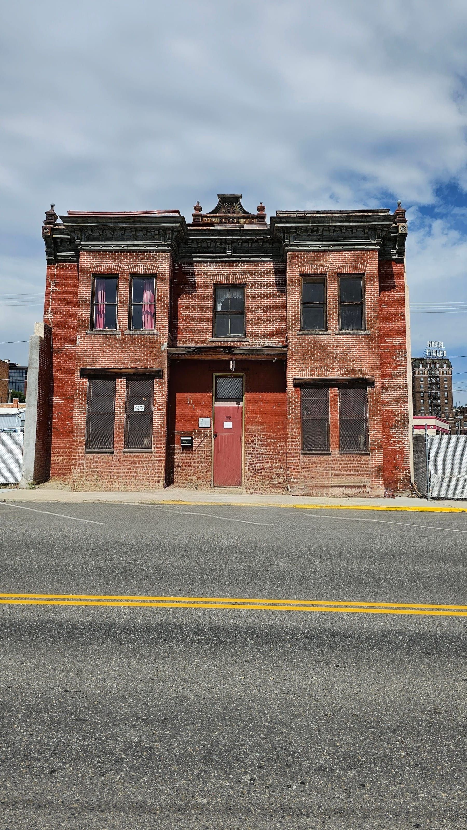 A historic 1890 red-brick building on a quiet street in Uptown Butte, Montana, under a wide cloudy sky